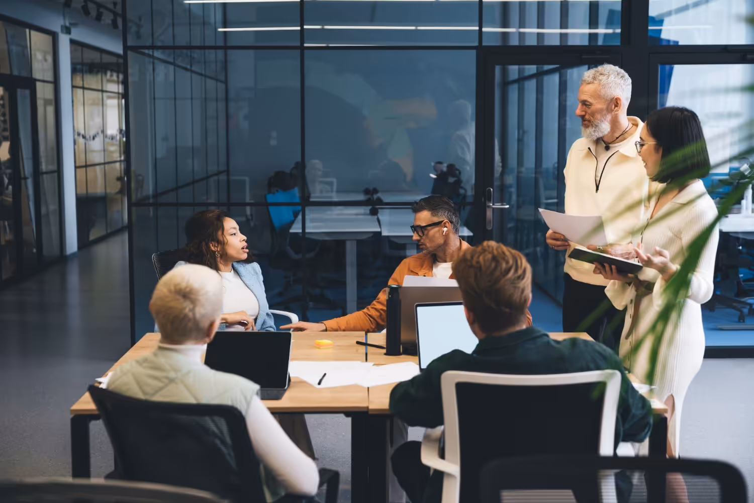 Business men and women having a meeting in an open plan office with glass walls.