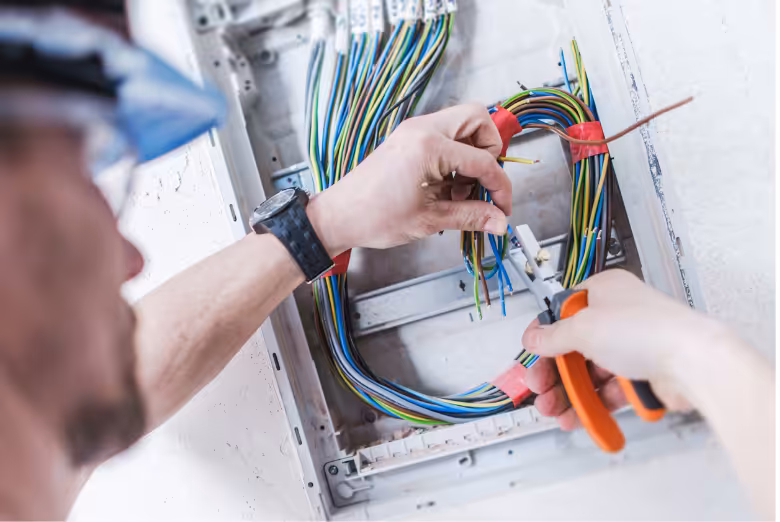 An engineer wearing a hard hat working on some cables in a wall recess.